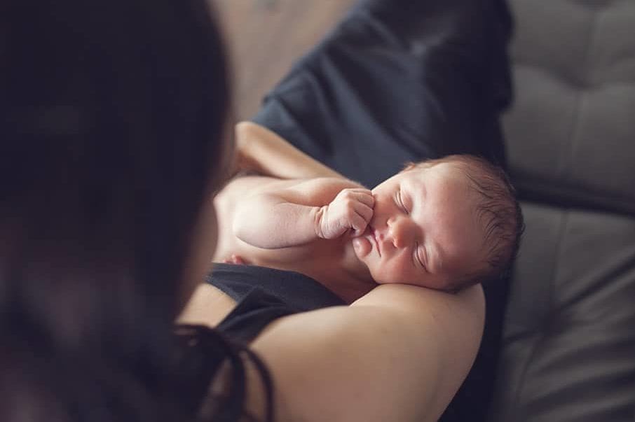 newborn baby in arms of mother on couch with window light