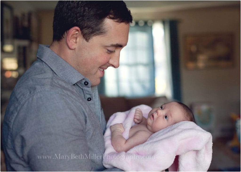 dad holding newborn baby girl in a soft pink plush blanket with window behind them