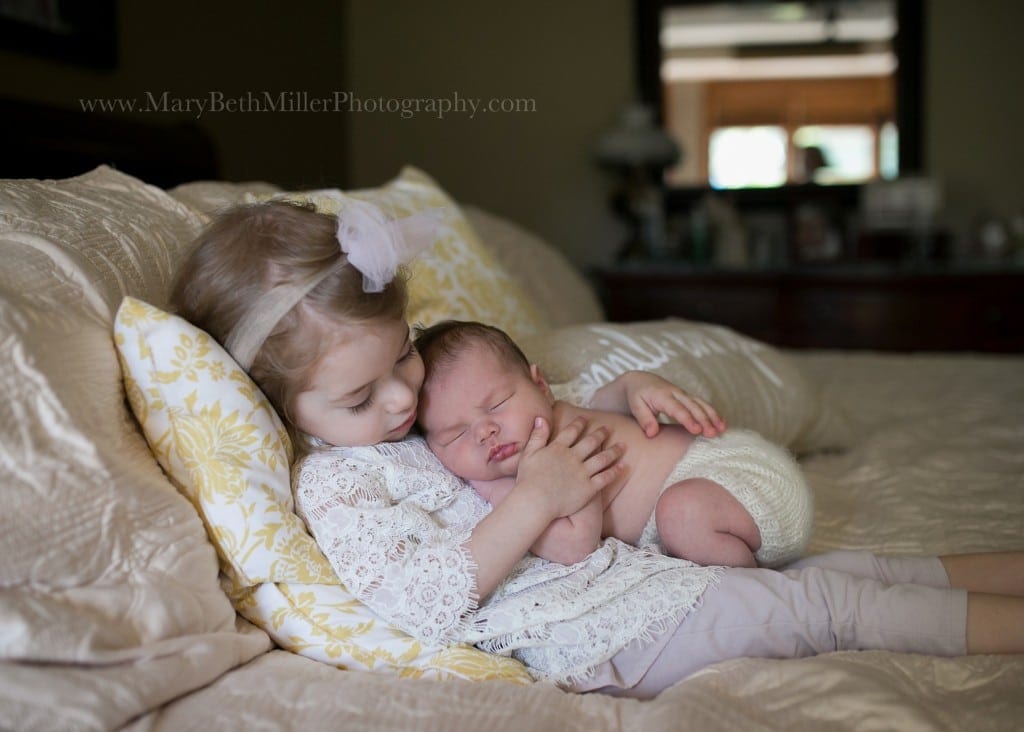 toddler girl holding her newborn baby brother on her chest on bad in bedroom for a newborn photo session  How to Find a Newborn Photographer in Pittsburgh