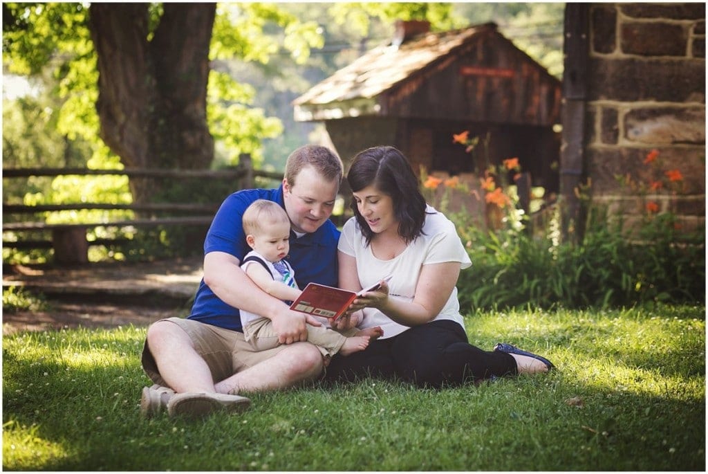 mother father and son on his lap reading a book in the grass for a picture
