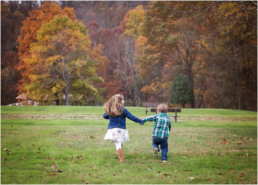 Brother and sister holding hands running through a grassy field with fall foliage trees in the background Pittsburgh Family Photographer | Mary Beth Miller Photography | Murrysville family photo session Townsend park