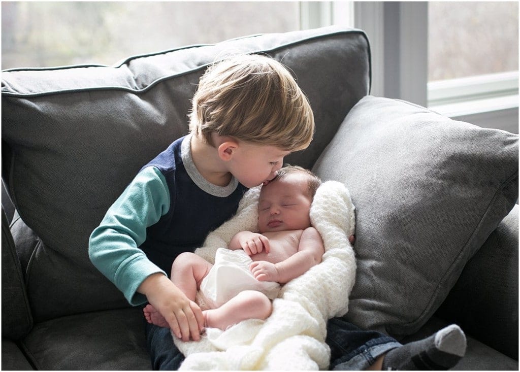 brother kissing sister on couch in front of window for a beaver newborn photo session
