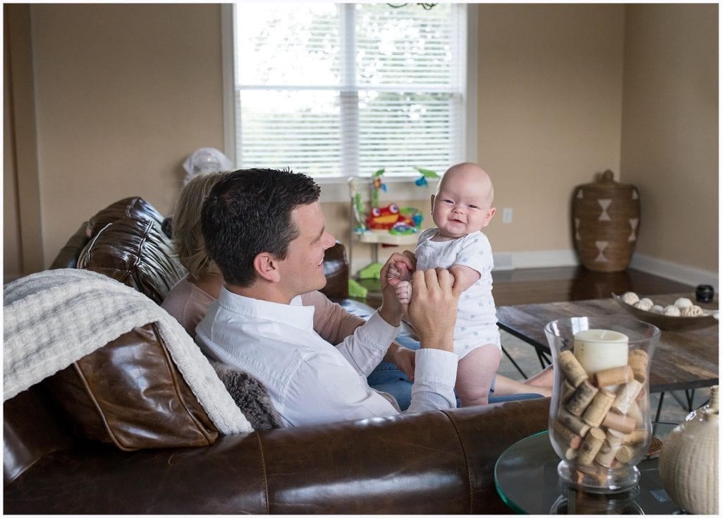 dad holding a standing and smiling baby on his lap on the couch in living room 