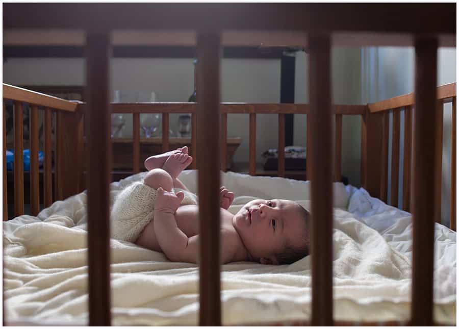 newborn baby girl laying in crib on cream blanket