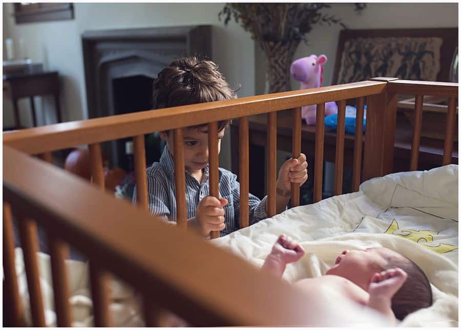 big brother looks at newborn sister in crib