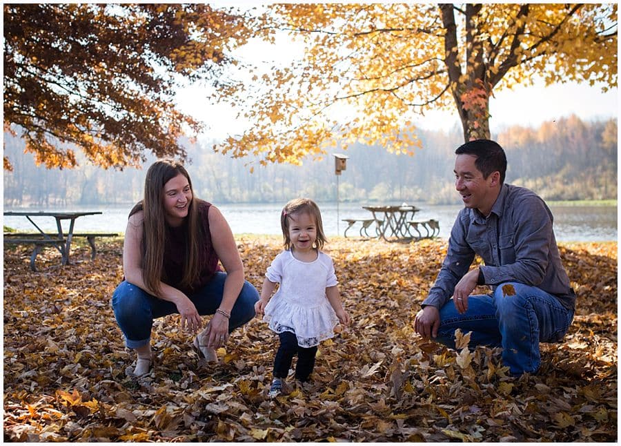 father mother and daughter in fall leaves playing in pittsburgh park