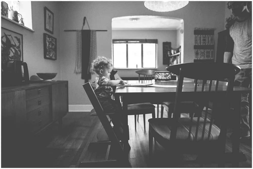 black and white image child sitting at the table in window light in home 