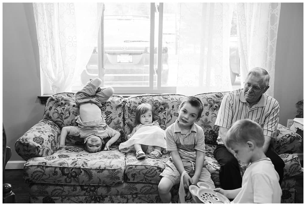black and white photo of toddler girl brother on his head on couch grandfather