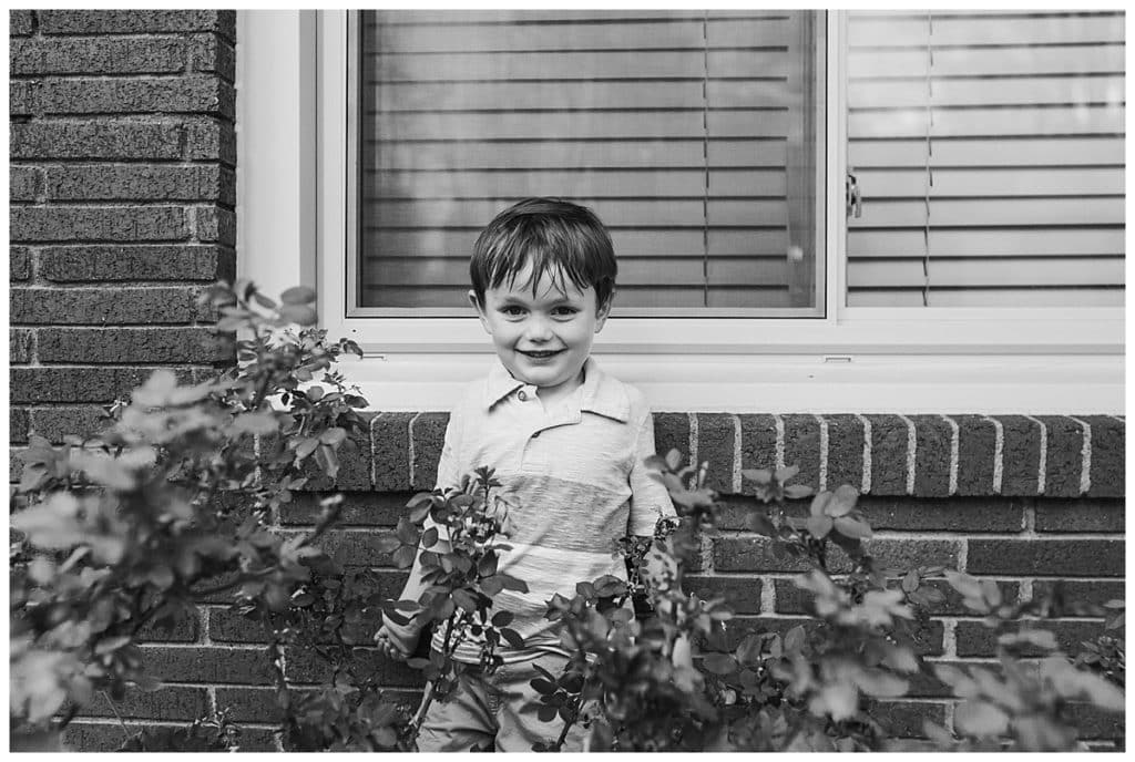 black and white photo of little boy by brick wall