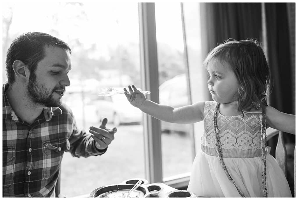 black and white photo of toddler girl feeding dad at table