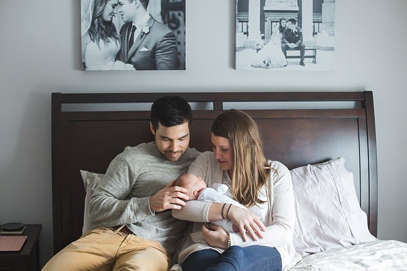mom and dad holding newborn baby on bed at home in pittsburgh