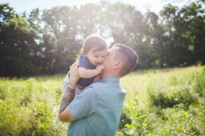 father kissing baby son in a pittsburgh field of wildflowers at sunset