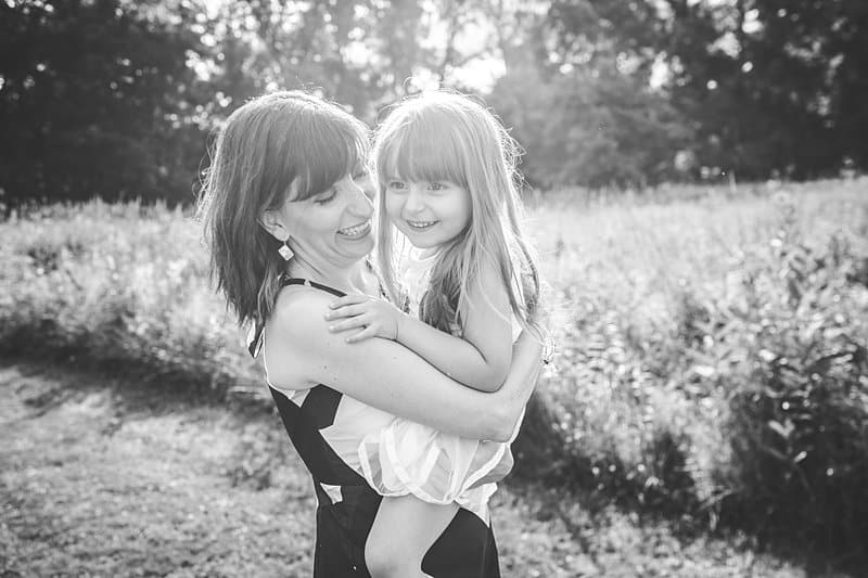 mother holding daughter in field with wildflowers at sunset in black and white