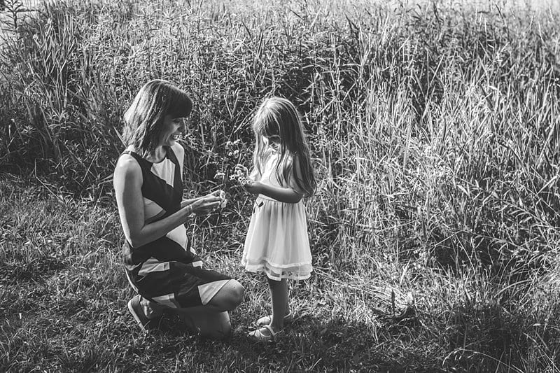 mother kneeling with daughter in field with wildflowers at sunset in black and white