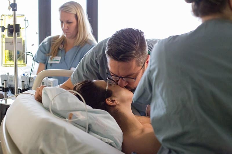 dad kissing mom in hospital bed birth session in pittsburgh