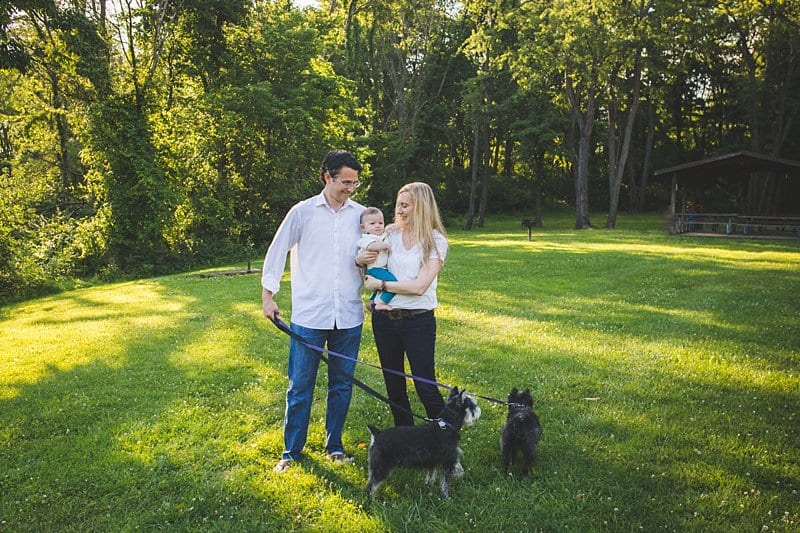 mom and dad holding baby girl at pittsburgh park with dogs