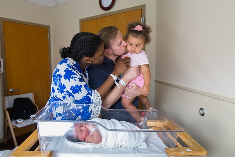 mom and dad and sister at magee hospital with newborn and in bassinet