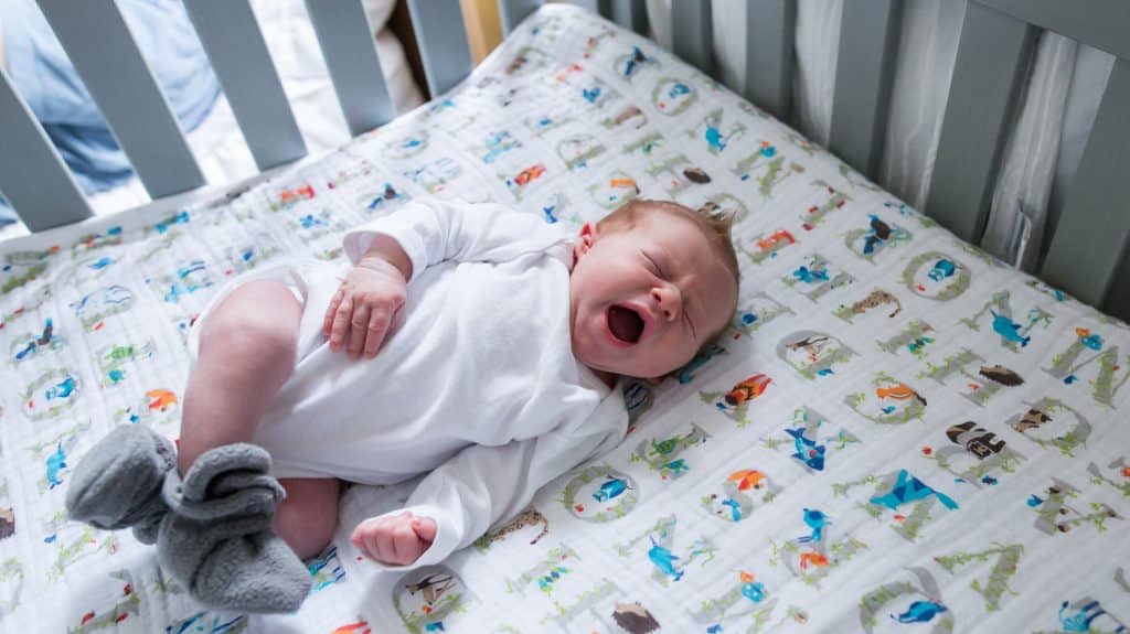 newborn baby in pittsburgh nursery yawing with gray fuzzy slippers and a white long sleeve onesie laying on alphabet sheets