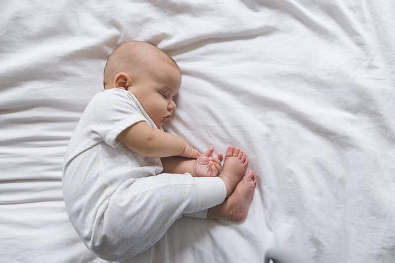 baby sleeping on bed finger toes chubby cheeks