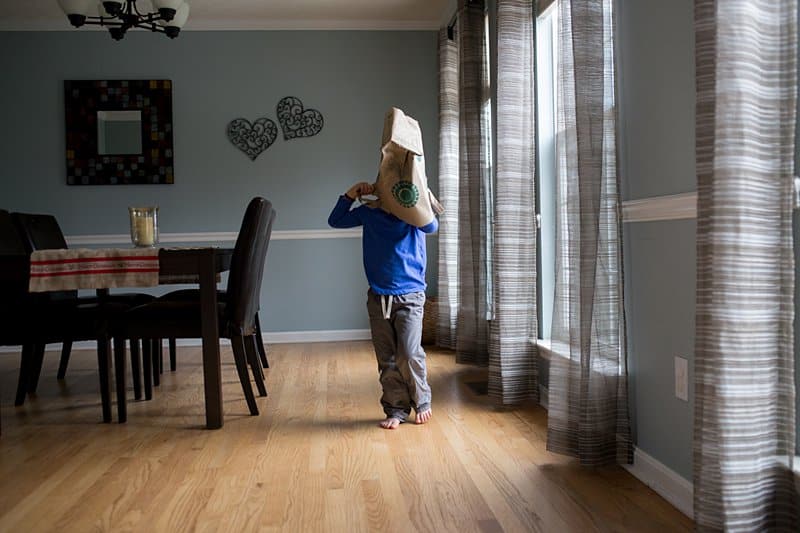 boy with a paper bag mask by window light