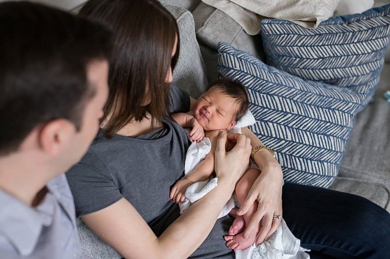 Mother holding smiling newborn baby on couch with dad sitting next to them