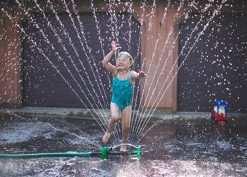 little girl jumping through sprinkler