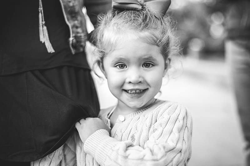 little girl holding moms skirt smiling