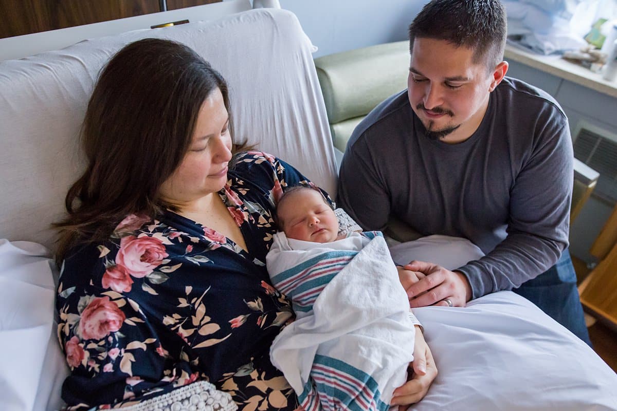 mom and dad holding newborn baby in hospital room bed