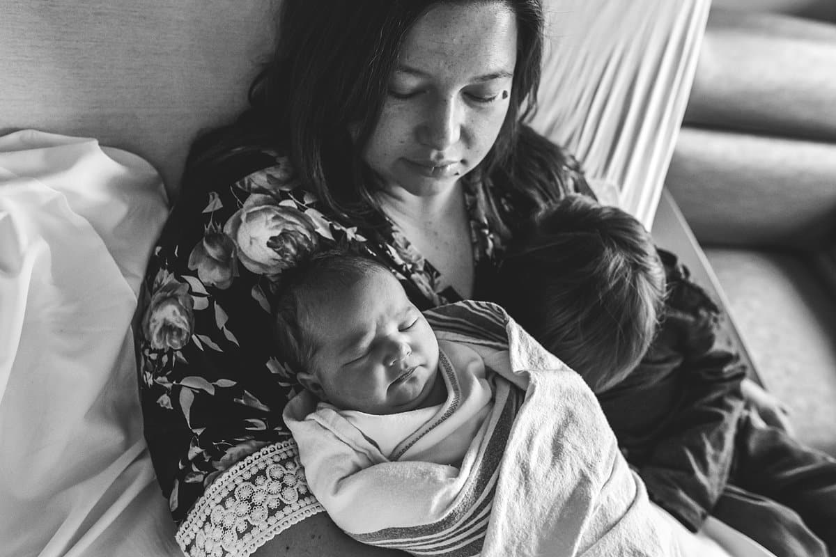 mom holding newborn baby in hospital room bed