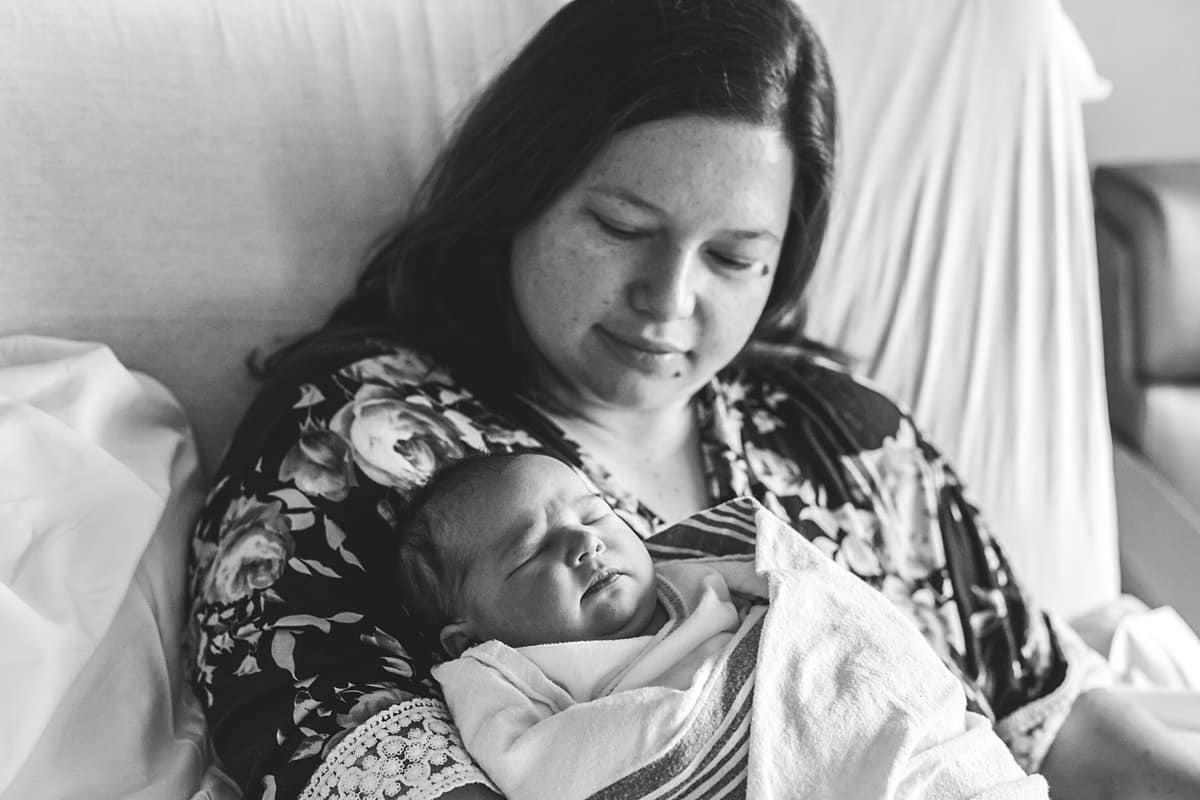 mom holding newborn baby in hospital room bed