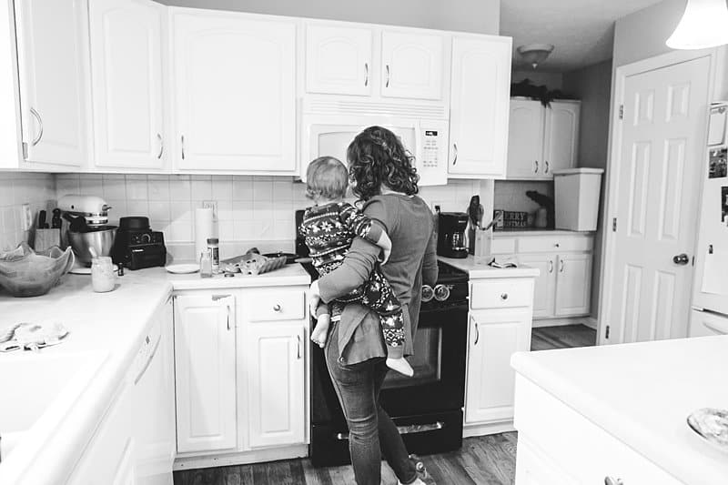 mom holding toddler in kitchen while cooking at stove
