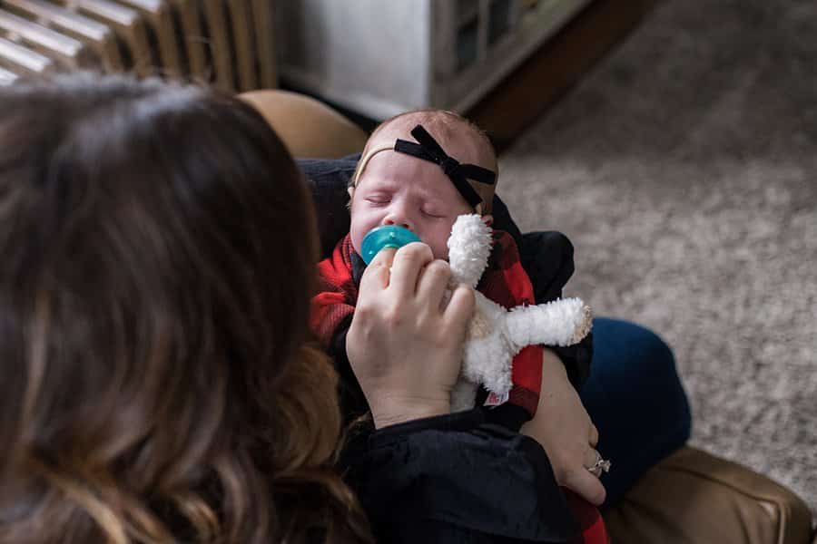 new mom holding her newborn daughter with a wubba nub pacifier in pittsburgh home