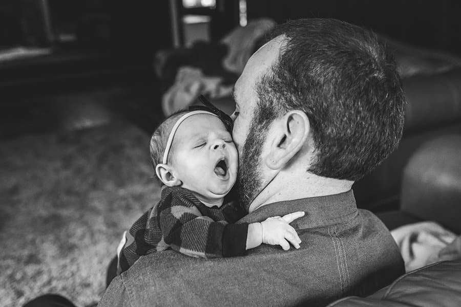 dad with newborn baby over shoulder yawning