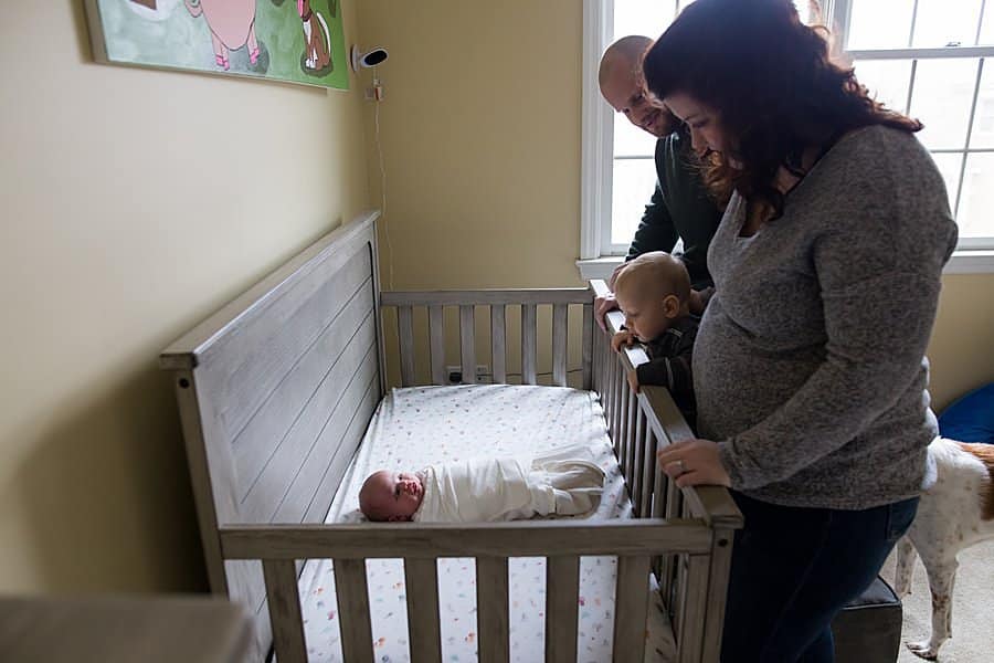 family looking over at newborn baby in crib in pittsburgh home nursery