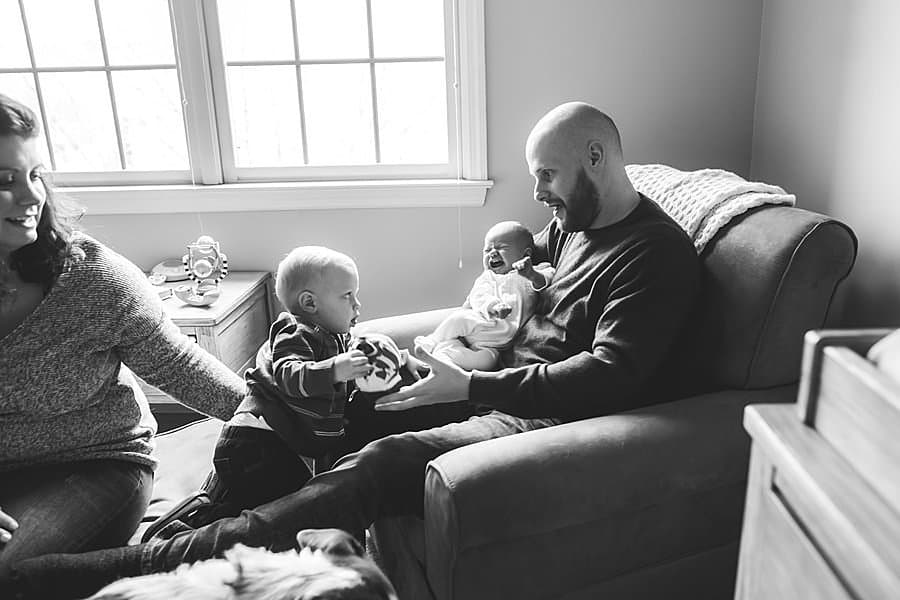 family sitting in baby nursery in pittsburgh home with dog toddler and newborn Tips for Including Toddler Siblings in Newborn Photos