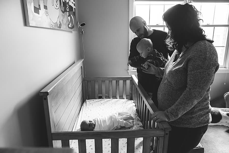 family looking over at newborn baby in crib in pittsburgh home nursery