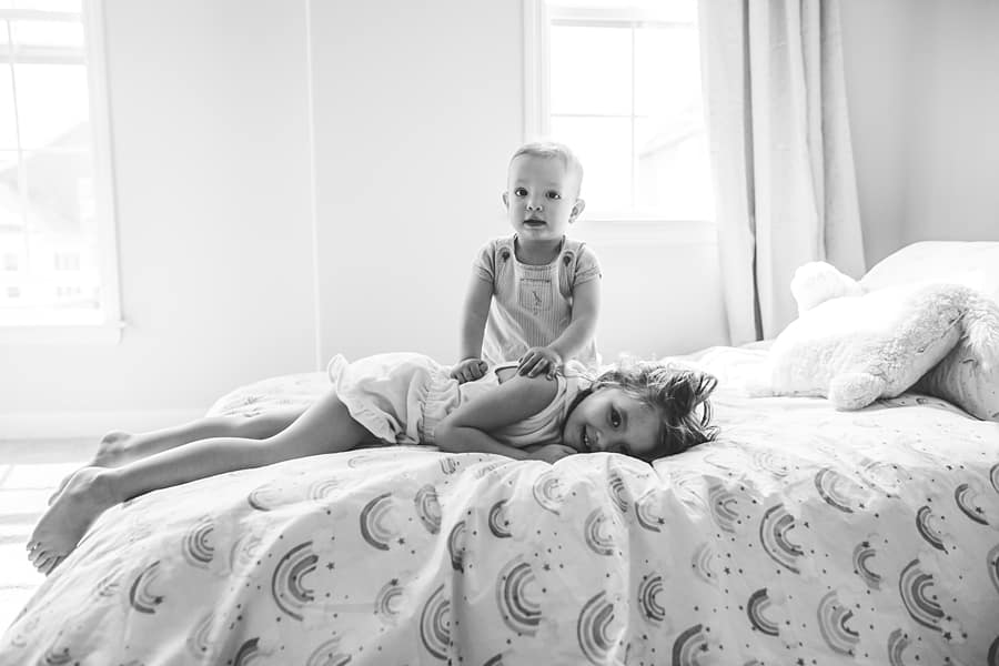 brother and sister playing on bed in window light for family photo session