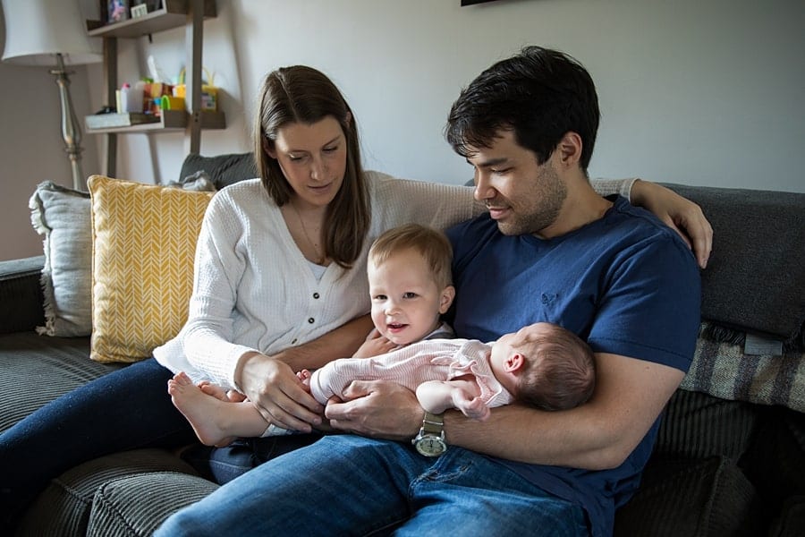 family with toddler and newborn sitting on couch of pittsburgh home for newborn photo session
