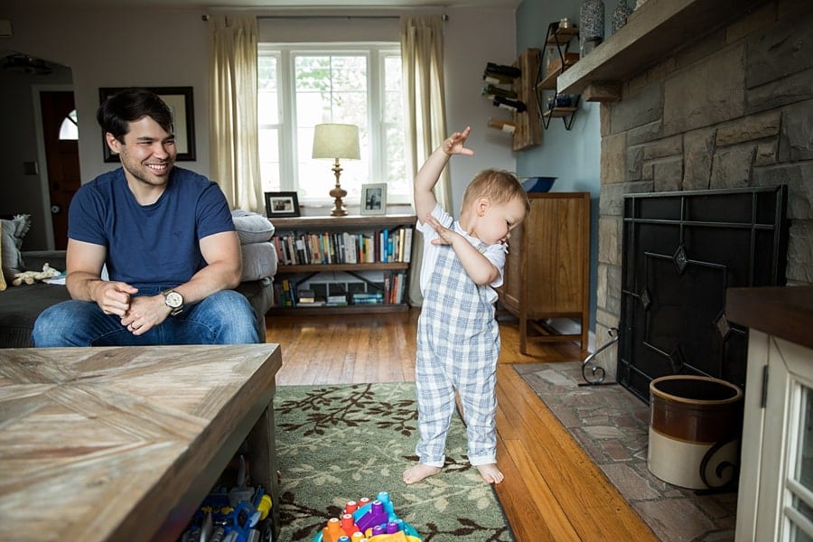 dad with dancing toddler sitting on couch of pittsburgh home for newborn photo session