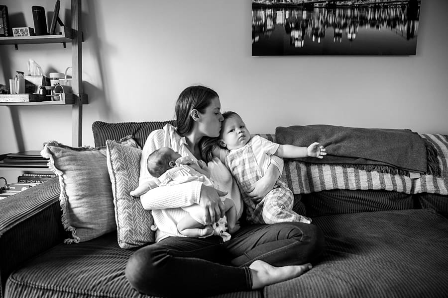 mom with toddler and newborn sitting on couch of pittsburgh home for newborn photo session Tips for Including Toddler Siblings in Newborn Photos
