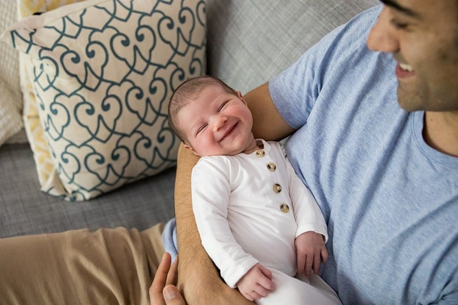 dad holding smiling newborn baby on couch of pittsburgh home