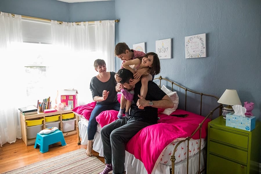 daughter and son climbing on dad in bedroom with pink bedspread Documentary Family Photos in Point Breeze Pittsburgh 