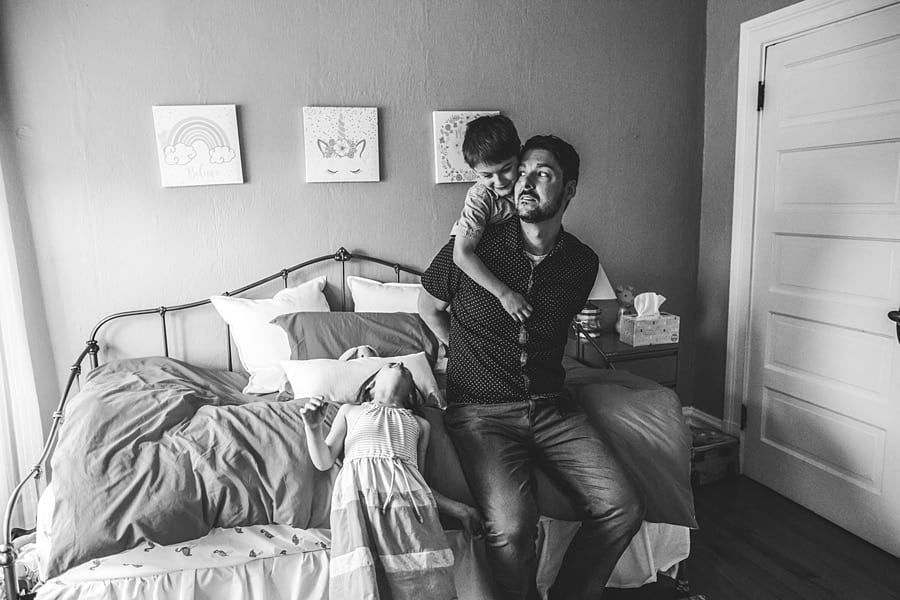 son hugging on dad's shoulders in bedroom with pink bedspread