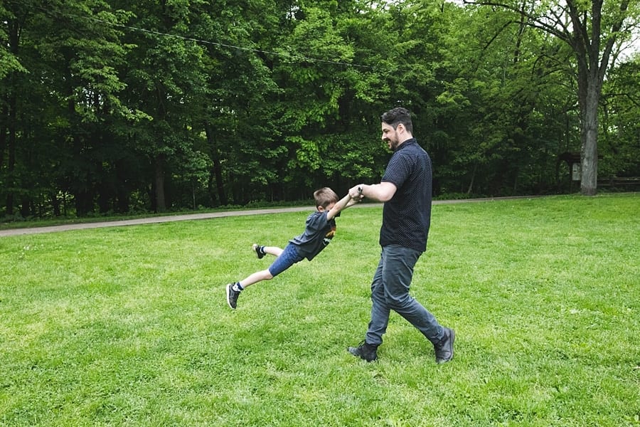 dad spinning son in green grass at frick park Family Photographer in Point Breeze Pittsburgh