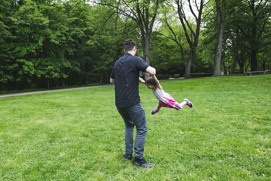 dad spinning daughter in green grass at frick park pittsburgh