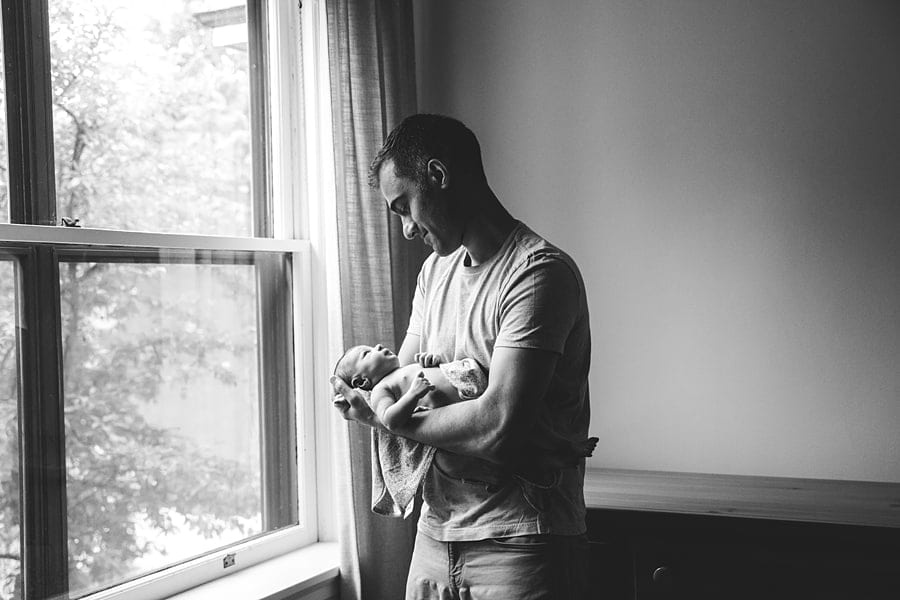 dad holding newborn daughter by the window light in the nursery of their Youngstown home