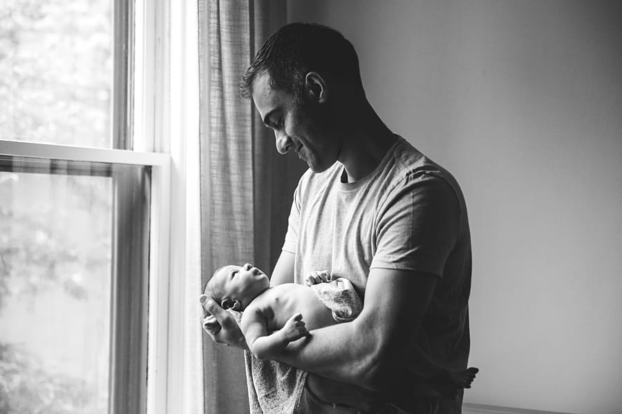 dad holding newborn daughter by the window light in the nursery of their shadyside home