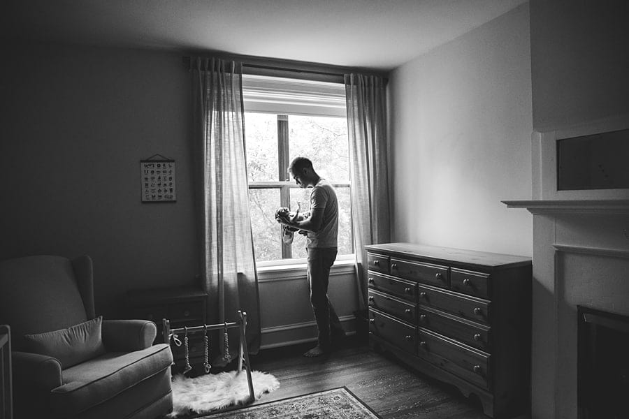dad holding newborn daughter by the window light in the nursery of their shadyside home