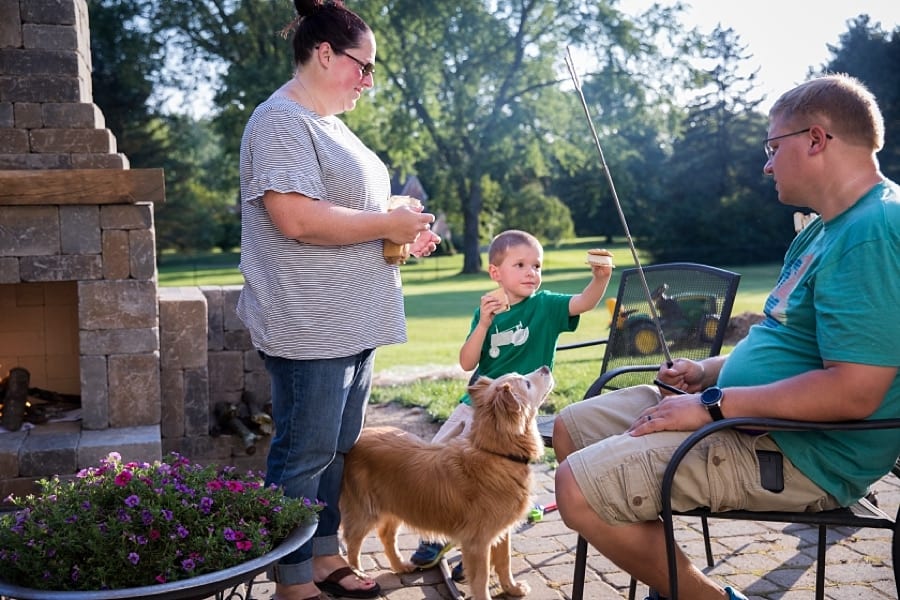 little boy offers dad a smores on their patio with dog and mom