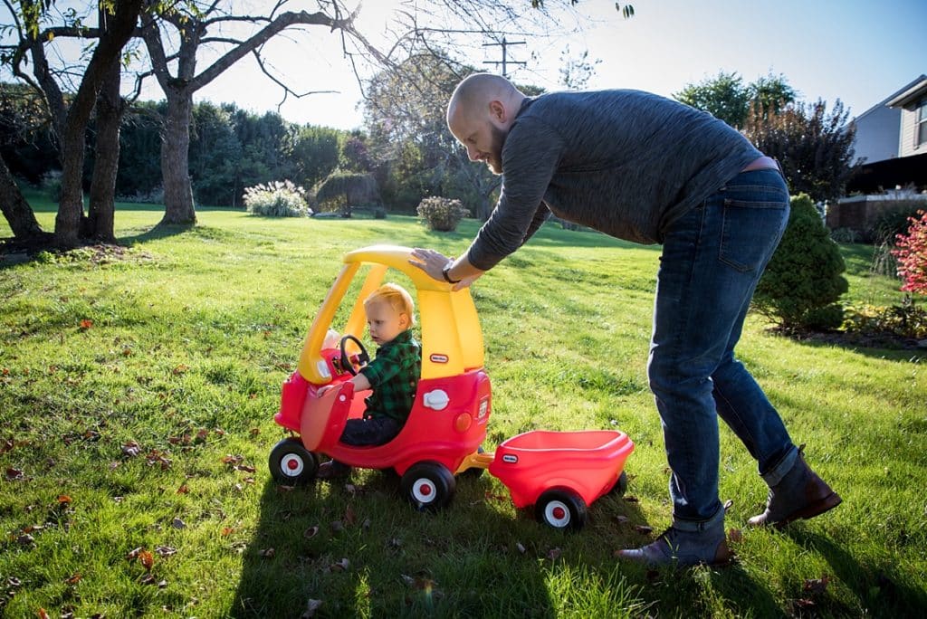 toddler boy in cozy coupe car outside in backyard for a fun and stress free family photo session